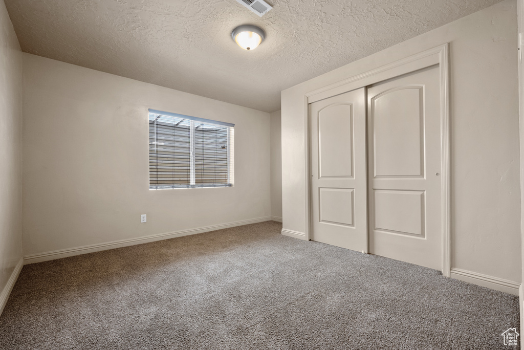 Unfurnished bedroom featuring a textured ceiling, carpet, and a closet