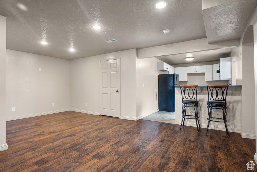 Kitchen featuring a textured ceiling, freestanding refrigerator, wood finished floors, a kitchen breakfast bar, and a peninsula