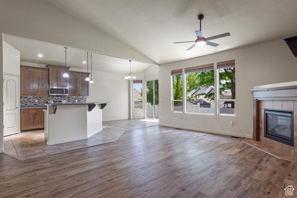 Unfurnished living room with wood finished floors, a ceiling fan, a chandelier, vaulted ceiling, and a tiled fireplace