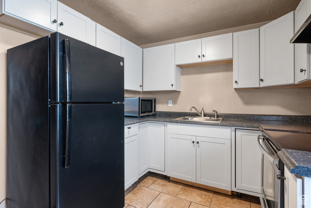 Kitchen with stainless steel appliances, dark countertops, white cabinets, exhaust hood, and a textured ceiling