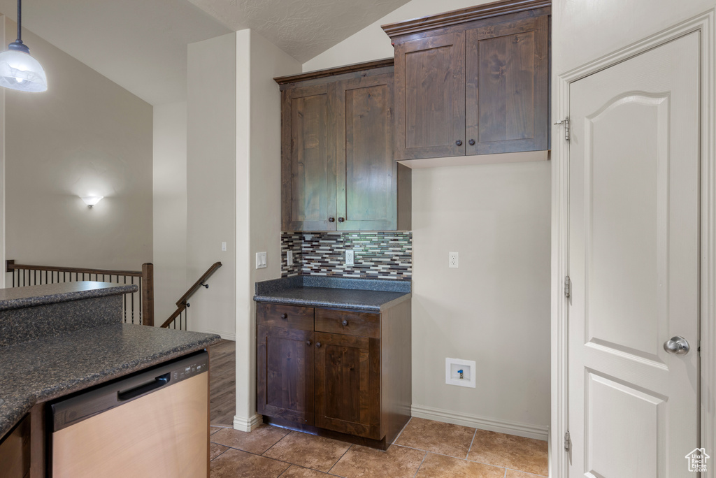 Kitchen featuring stainless steel dishwasher, dark countertops, backsplash, light tile patterned flooring, and dark brown cabinetry