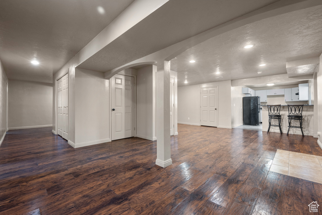 Below grade area featuring freestanding refrigerator, arched walkways, dark wood-style flooring, and recessed lighting