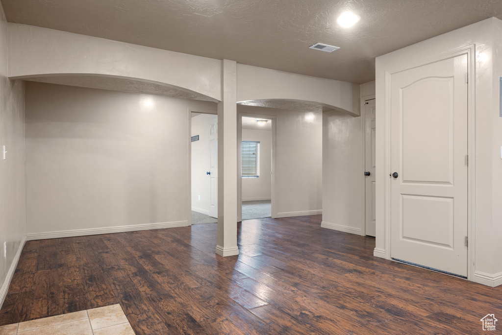 Below grade area with arched walkways, dark wood-style floors, and a textured ceiling