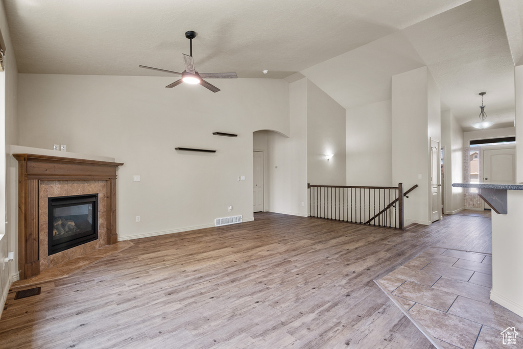 Unfurnished living room with ceiling fan, a tiled fireplace, wood finished floors, arched walkways, and high vaulted ceiling