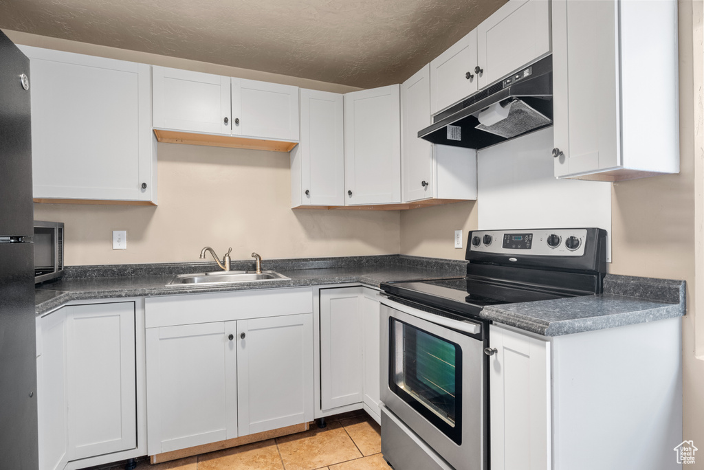 Kitchen with stainless steel range with electric stovetop, under cabinet range hood, white cabinetry, dark countertops, and a textured ceiling