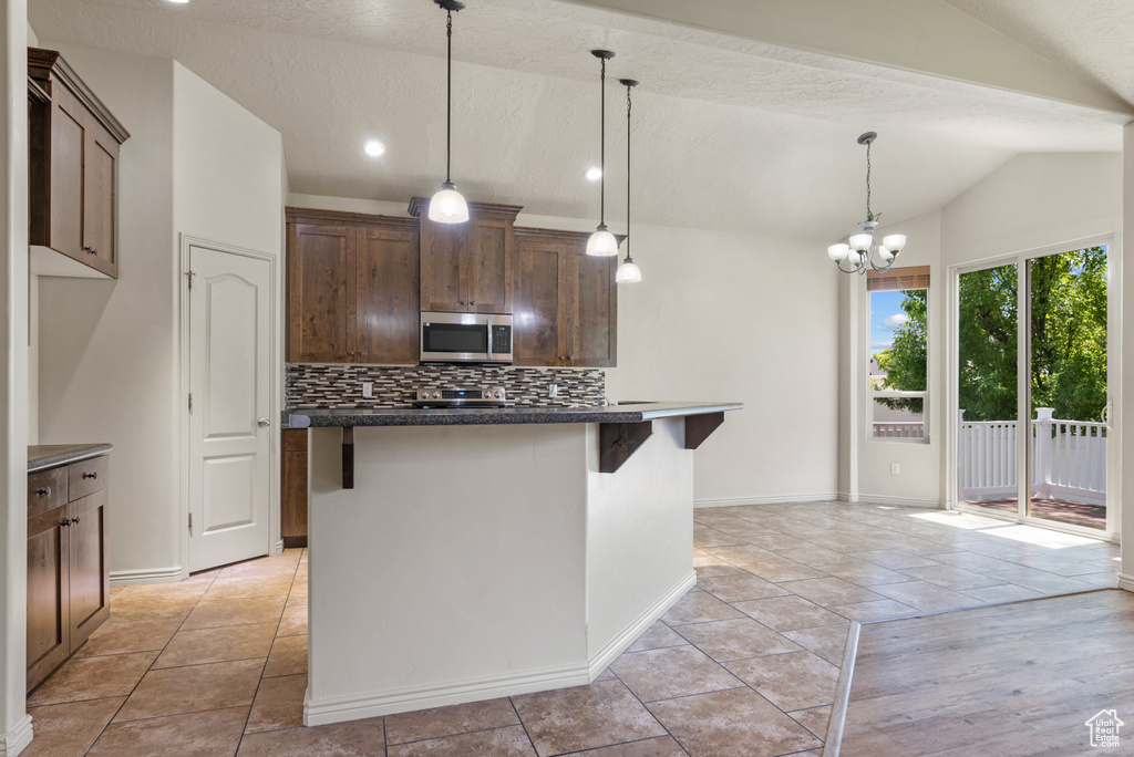 Kitchen with stainless steel microwave, lofted ceiling, dark countertops, tasteful backsplash, and a center island