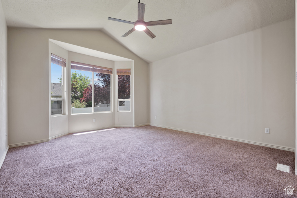Carpeted spare room with ceiling fan and vaulted ceiling