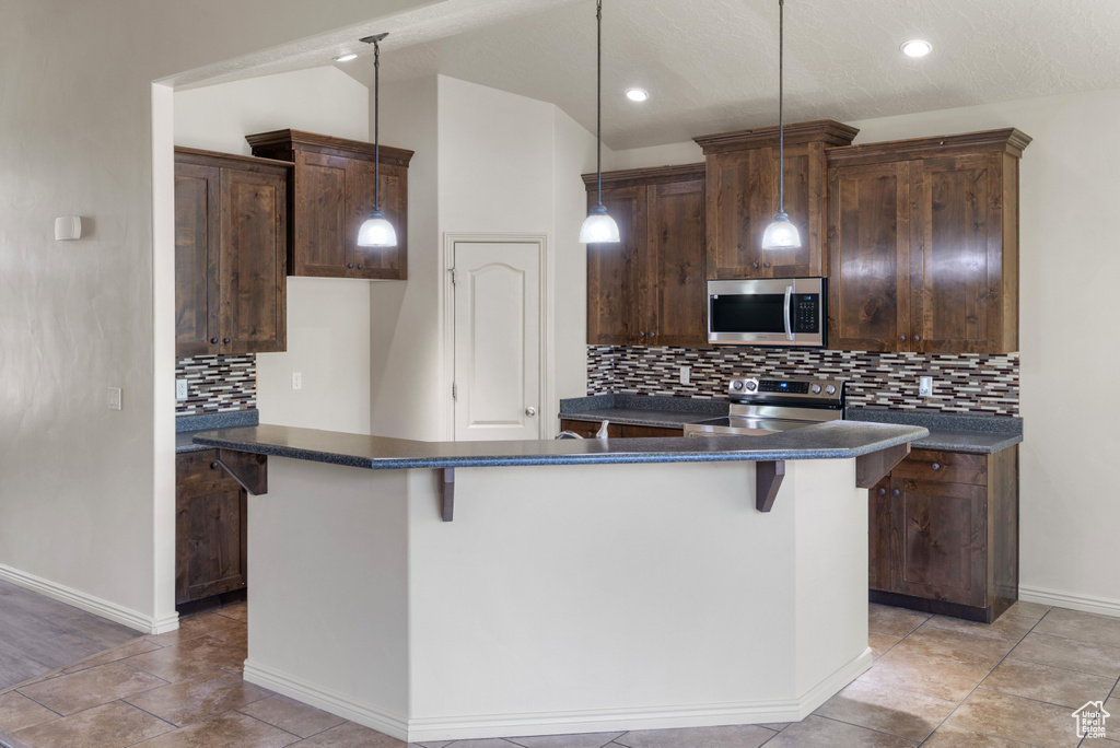 Kitchen featuring stainless steel appliances, dark countertops, a center island, decorative backsplash, and recessed lighting
