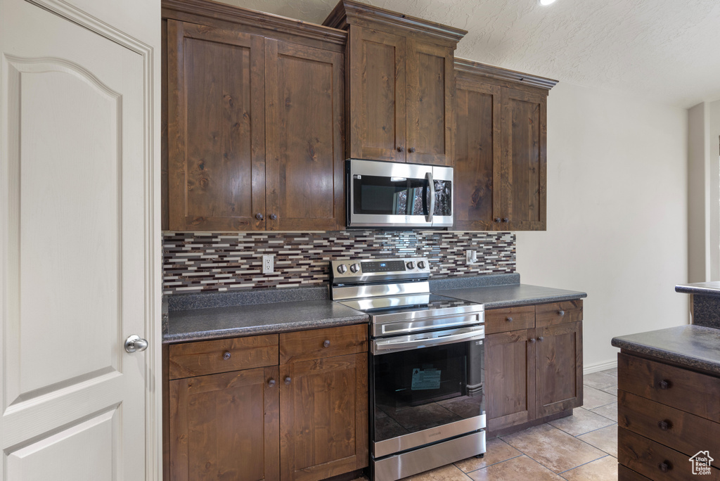 Kitchen featuring appliances with stainless steel finishes, dark countertops, tasteful backsplash, light tile patterned floors, and a textured ceiling