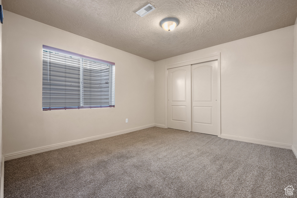 Unfurnished bedroom featuring a textured ceiling, carpet flooring, and a closet