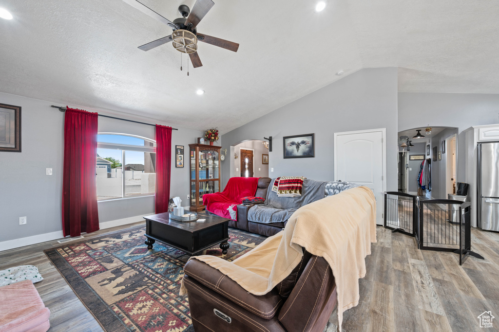 Living area with a ceiling fan, arched walkways, lofted ceiling, light wood-type flooring, and recessed lighting