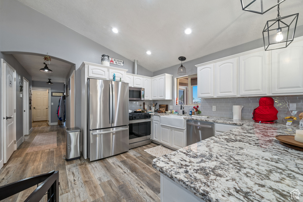 Kitchen with appliances with stainless steel finishes, light stone counters, decorative backsplash, arched walkways, and light wood finished floors