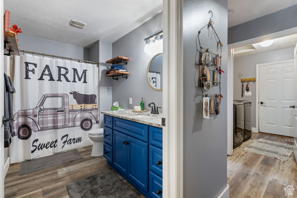 Full bath featuring independent washer and dryer, wood finished floors, vanity, a textured ceiling, and a shower with curtain