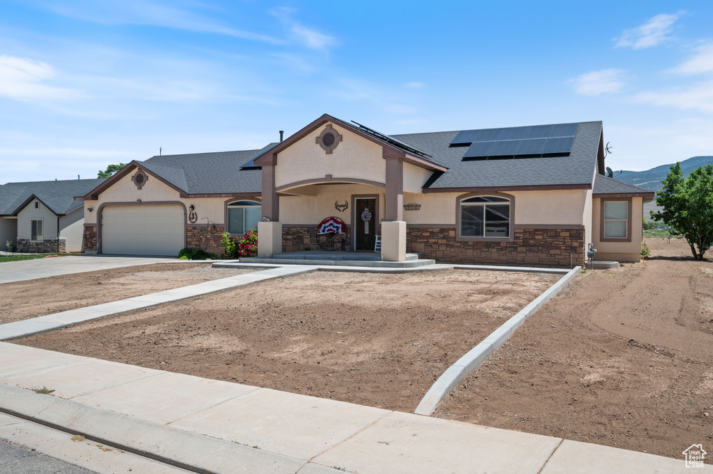 View of front of house with stone siding, stucco siding, roof with shingles, driveway, and solar panels