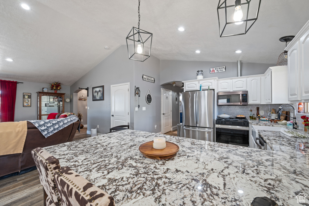 Kitchen featuring appliances with stainless steel finishes, wood finished floors, light stone countertops, white cabinets, and recessed lighting