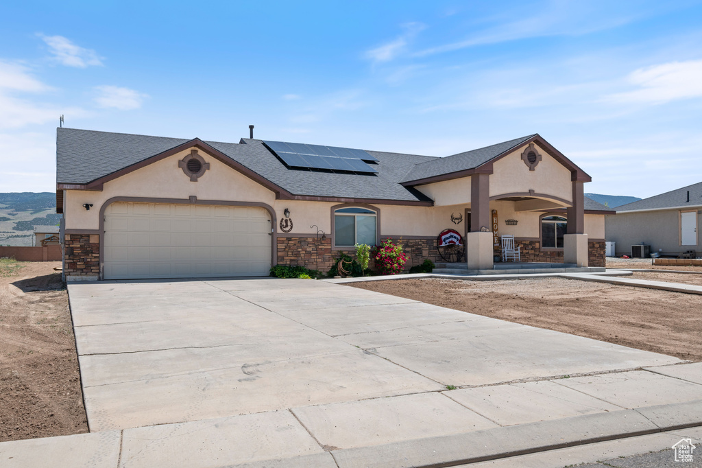 View of front facade featuring stone siding, stucco siding, roof mounted solar panels, and an attached garage