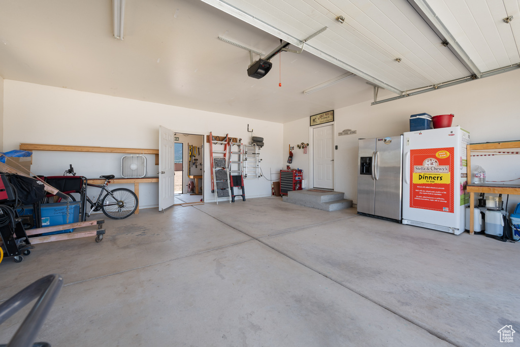 Garage with stainless steel fridge and a garage door opener