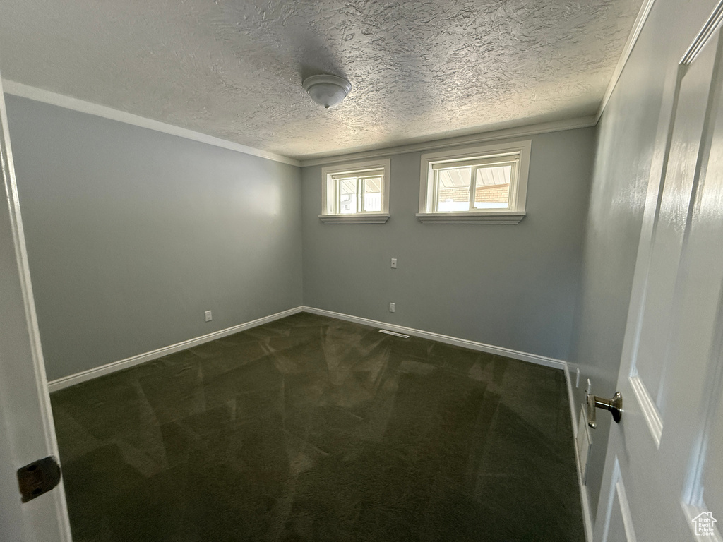Spare room featuring dark carpet, ornamental molding, and a textured ceiling