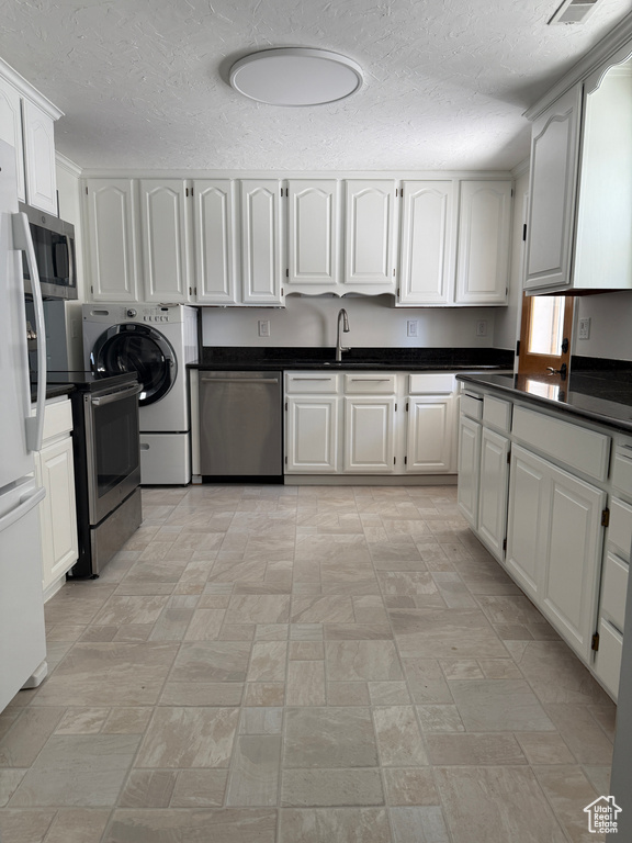 Kitchen featuring appliances with stainless steel finishes, washer / dryer, a textured ceiling, dark countertops, and white cabinetry