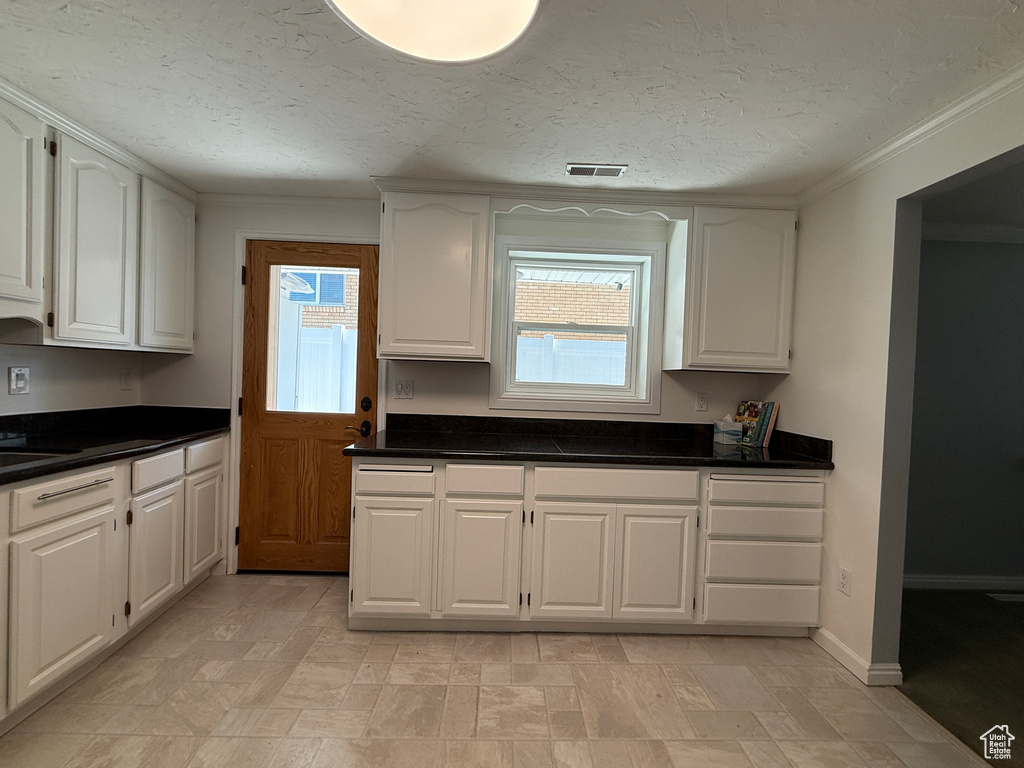 Kitchen featuring white cabinets, dark countertops, ornamental molding, and a textured ceiling