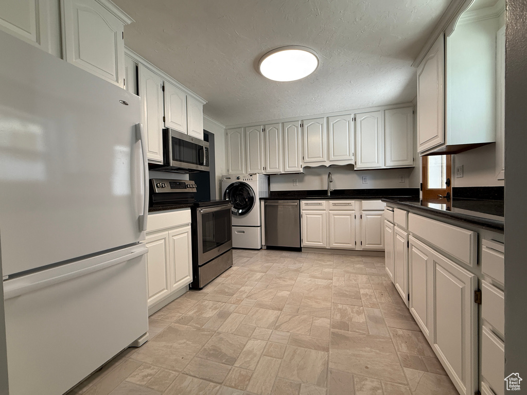 Kitchen with appliances with stainless steel finishes, washer / dryer, dark countertops, a textured ceiling, and white cabinets