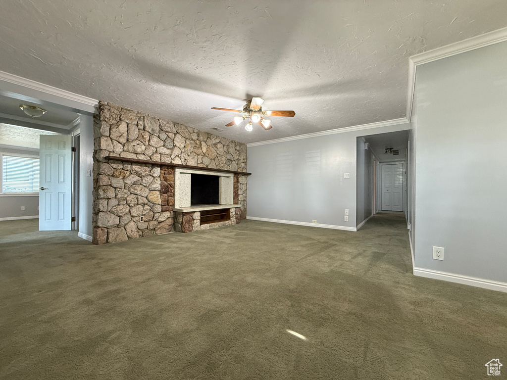 Unfurnished living room featuring ornamental molding, ceiling fan, carpet flooring, a fireplace, and a textured ceiling