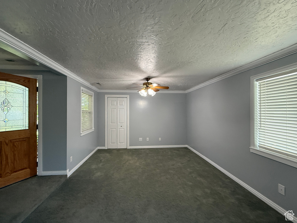 Entrance foyer with ceiling fan, dark colored carpet, a textured ceiling, and ornamental molding