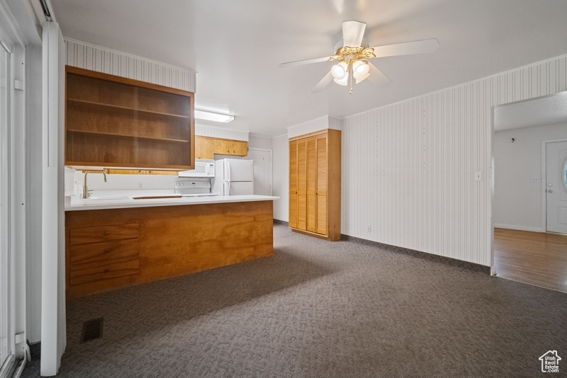 Kitchen featuring white appliances, a ceiling fan, dark carpet, and a peninsula