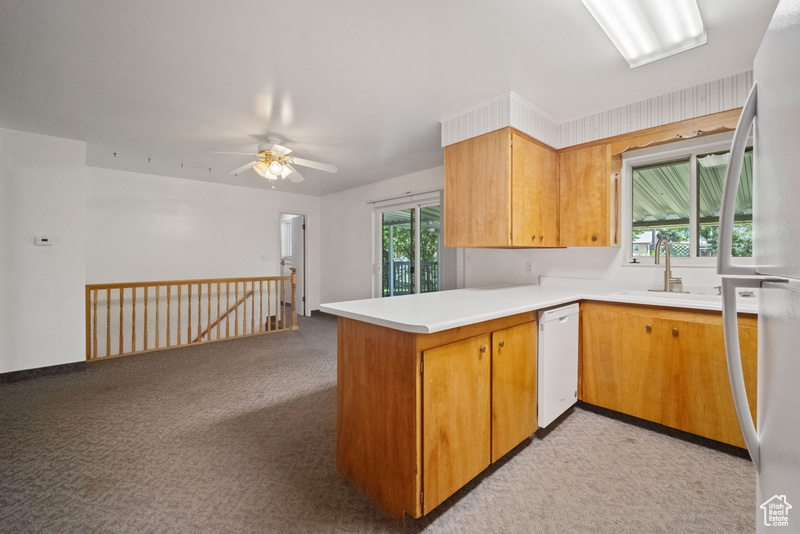 Kitchen featuring white appliances, a peninsula, light colored carpet, light countertops, and a ceiling fan