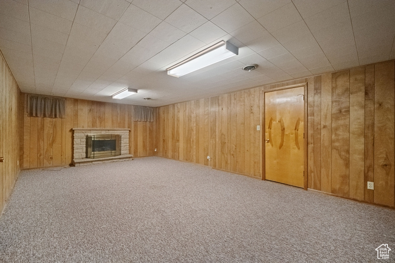 Unfurnished living room with wood walls, a stone fireplace, and carpet floors