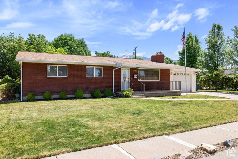 Ranch-style home featuring driveway, a garage, brick siding, and a chimney