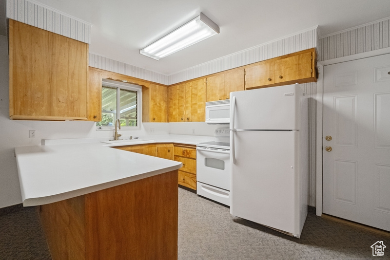 Kitchen with white appliances, a peninsula, light countertops, and light carpet