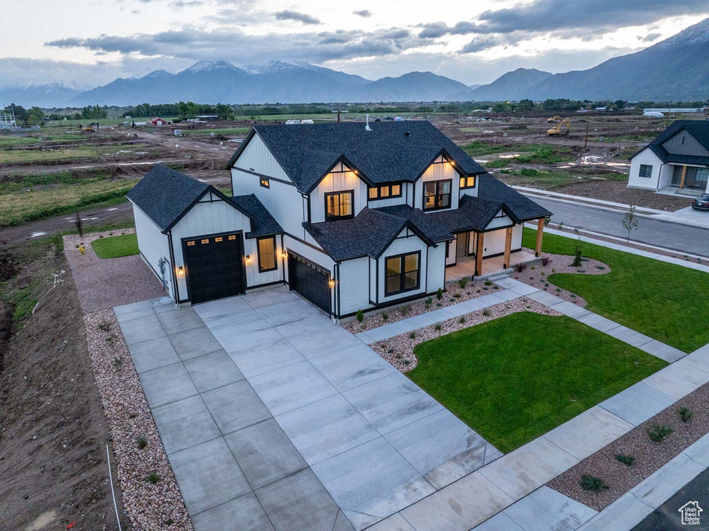 Modern farmhouse style home with a garage, a mountain view, roof with shingles, a front yard, and driveway