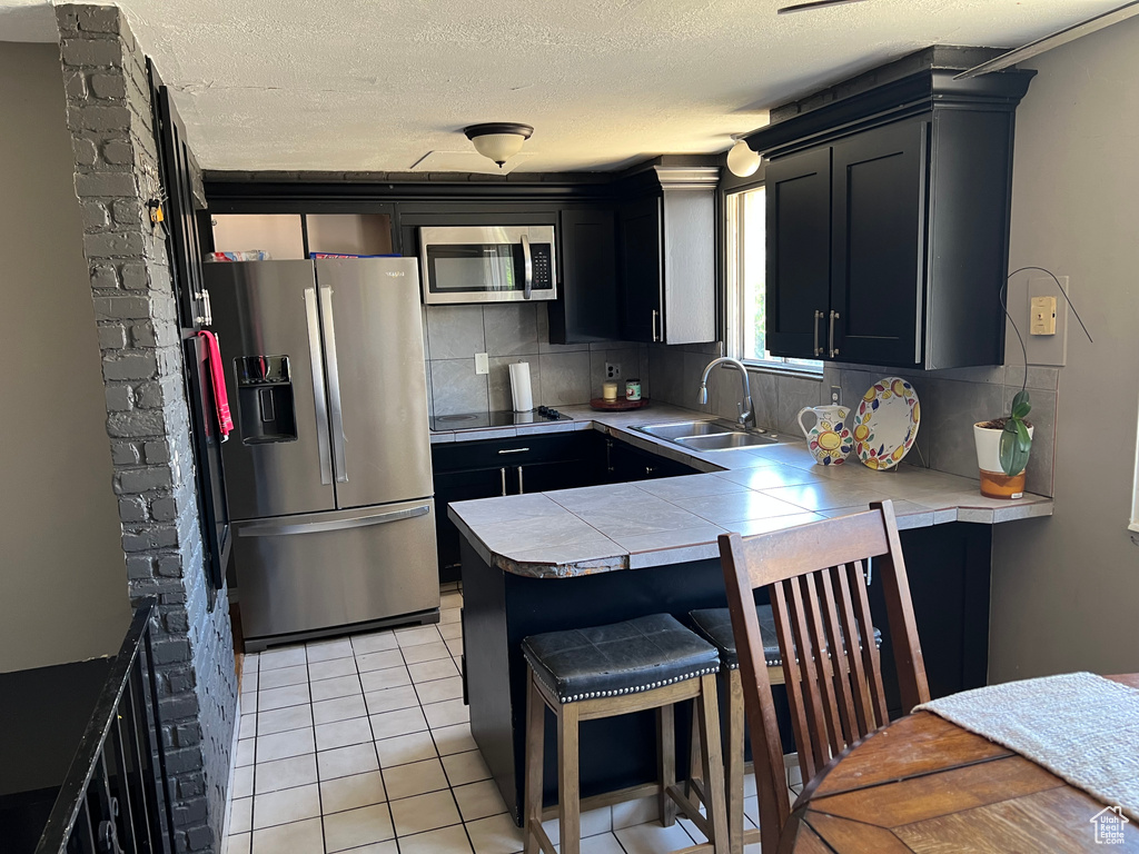 Kitchen with stainless steel appliances, dark cabinets, tasteful backsplash, a breakfast bar area, and a textured ceiling