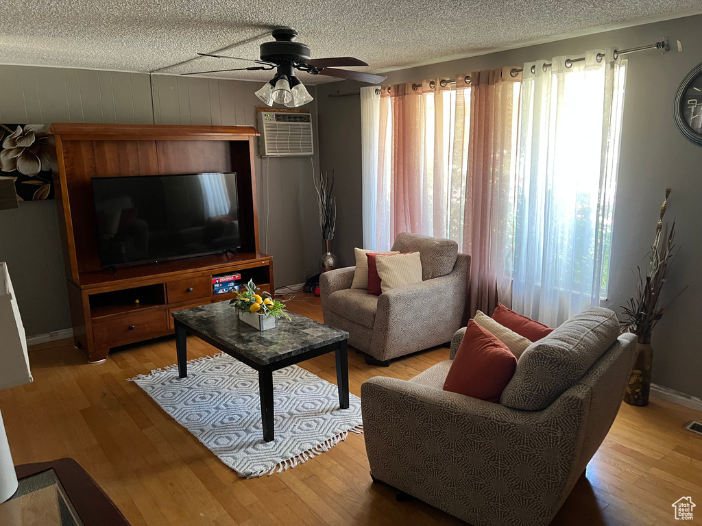 Living room featuring an AC wall unit, a ceiling fan, wood finished floors, and a textured ceiling