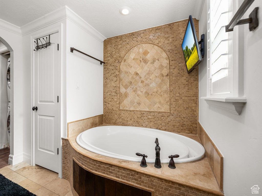 Full bath with stacked washer and clothes dryer, a garden tub, and crown molding