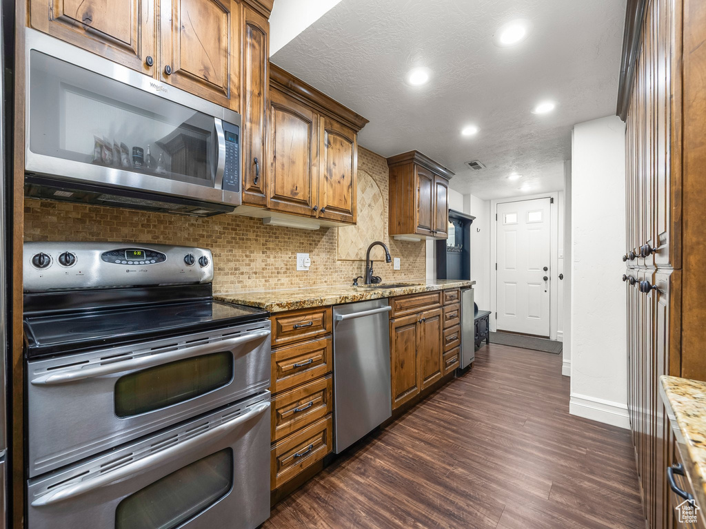 Kitchen with stainless steel appliances, backsplash, dark wood-type flooring, recessed lighting, and light stone countertops