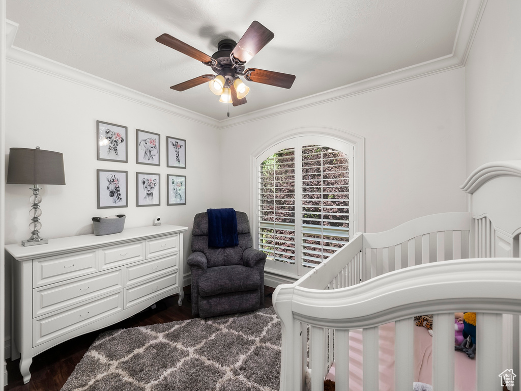 Bedroom featuring crown molding, dark wood-type flooring, a crib, and a ceiling fan