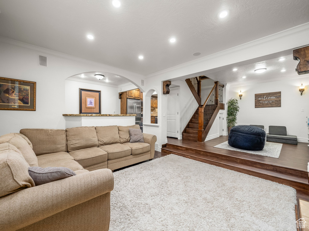 Living room featuring ornamental molding, arched walkways, wood finished floors, stairway, and recessed lighting