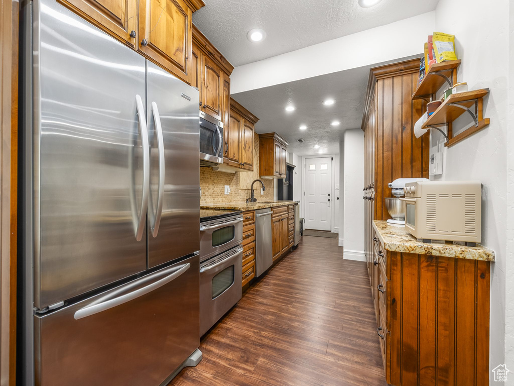 Kitchen featuring stainless steel appliances, dark wood finished floors, light stone countertops, backsplash, and recessed lighting
