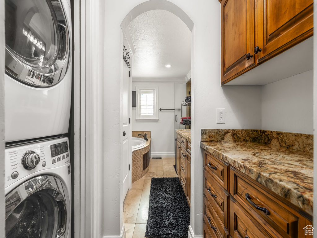 Washroom with stacked washing machine and dryer, arched walkways, and crown molding