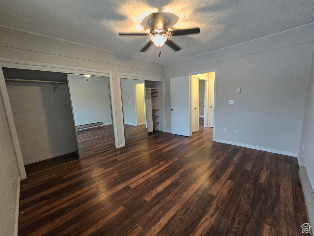 Unfurnished bedroom with two closets, dark wood-type flooring, a baseboard radiator, and ceiling fan
