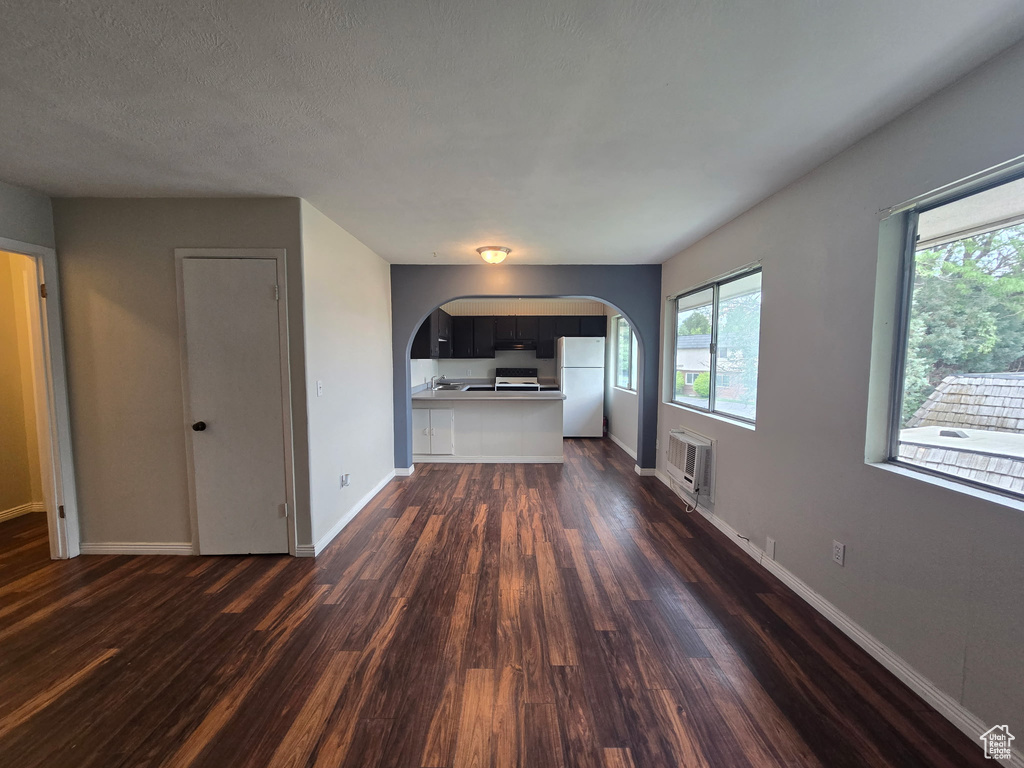 Unfurnished living room with arched walkways, dark wood-style flooring, and healthy amount of natural light