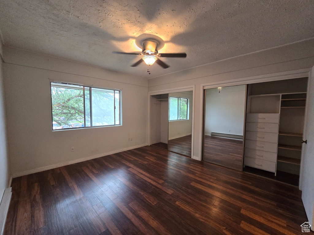 Unfurnished bedroom featuring multiple closets, baseboard heating, dark wood-type flooring, a textured ceiling, and a ceiling fan