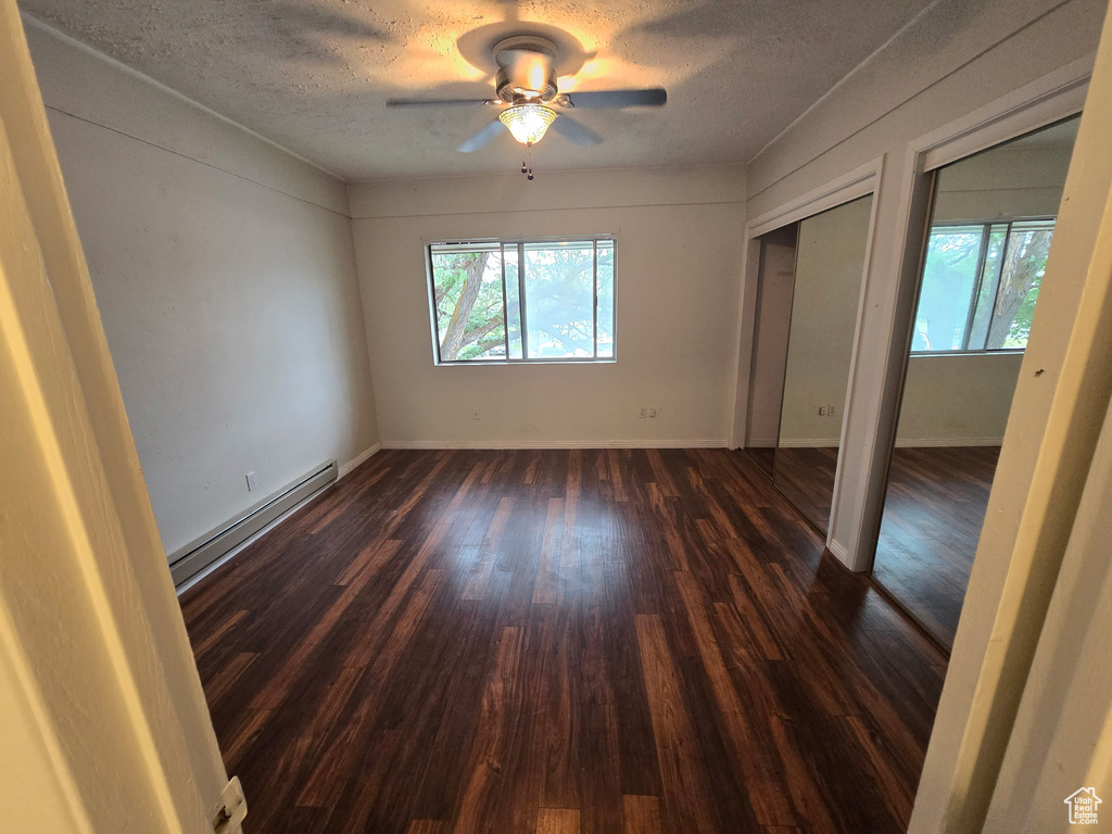 Empty room featuring a baseboard radiator, plenty of natural light, dark wood-type flooring, a textured ceiling, and a ceiling fan