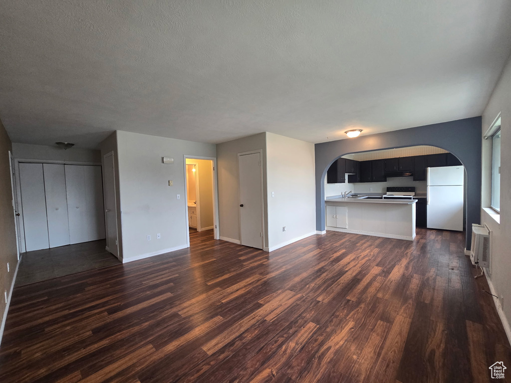 Unfurnished living room with dark wood finished floors, arched walkways, an AC wall unit, and a textured ceiling