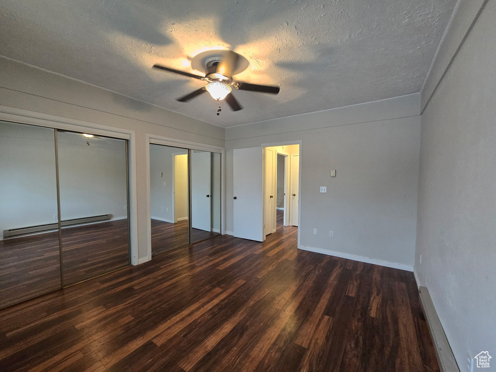 Unfurnished bedroom featuring a baseboard radiator, multiple closets, dark wood-type flooring, a textured ceiling, and ceiling fan