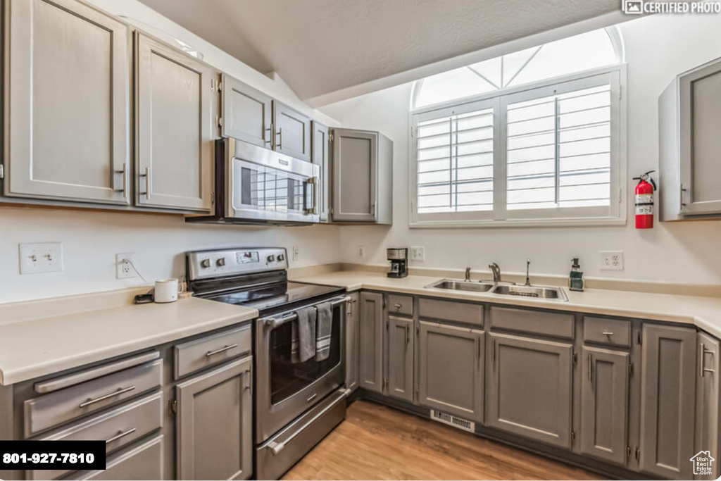 Kitchen featuring appliances with stainless steel finishes, gray cabinets, vaulted ceiling, light countertops, and light wood-style flooring