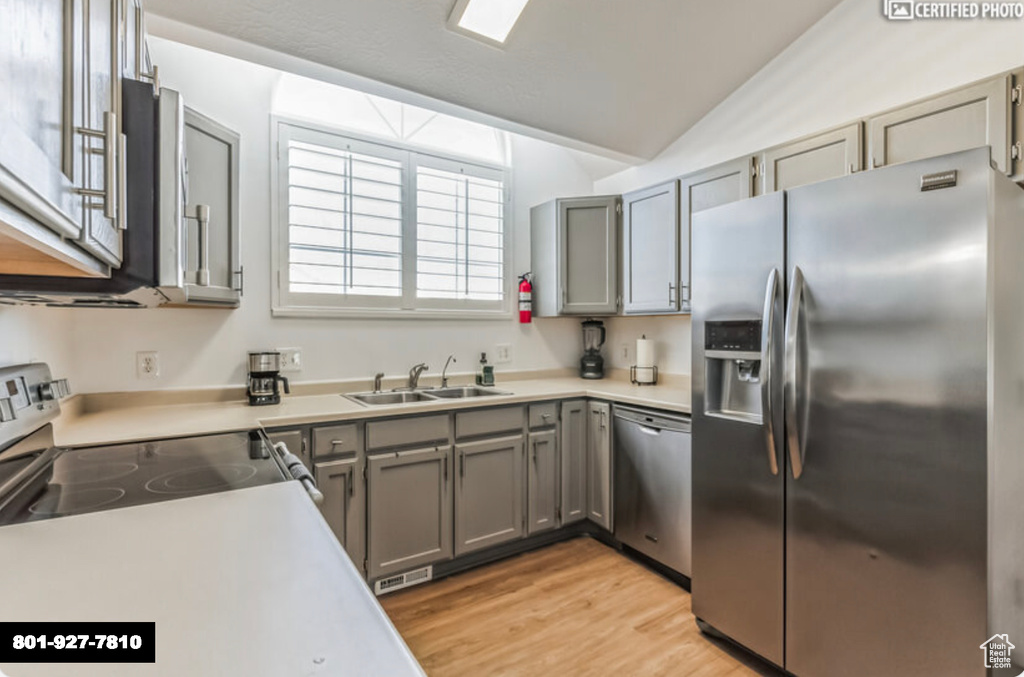 Kitchen featuring stainless steel appliances, gray cabinetry, lofted ceiling, light wood-style floors, and light countertops