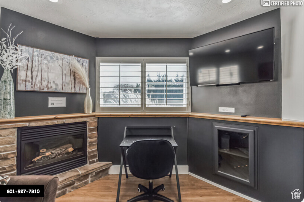 Home office featuring wood finished floors, a glass covered fireplace, and a textured ceiling